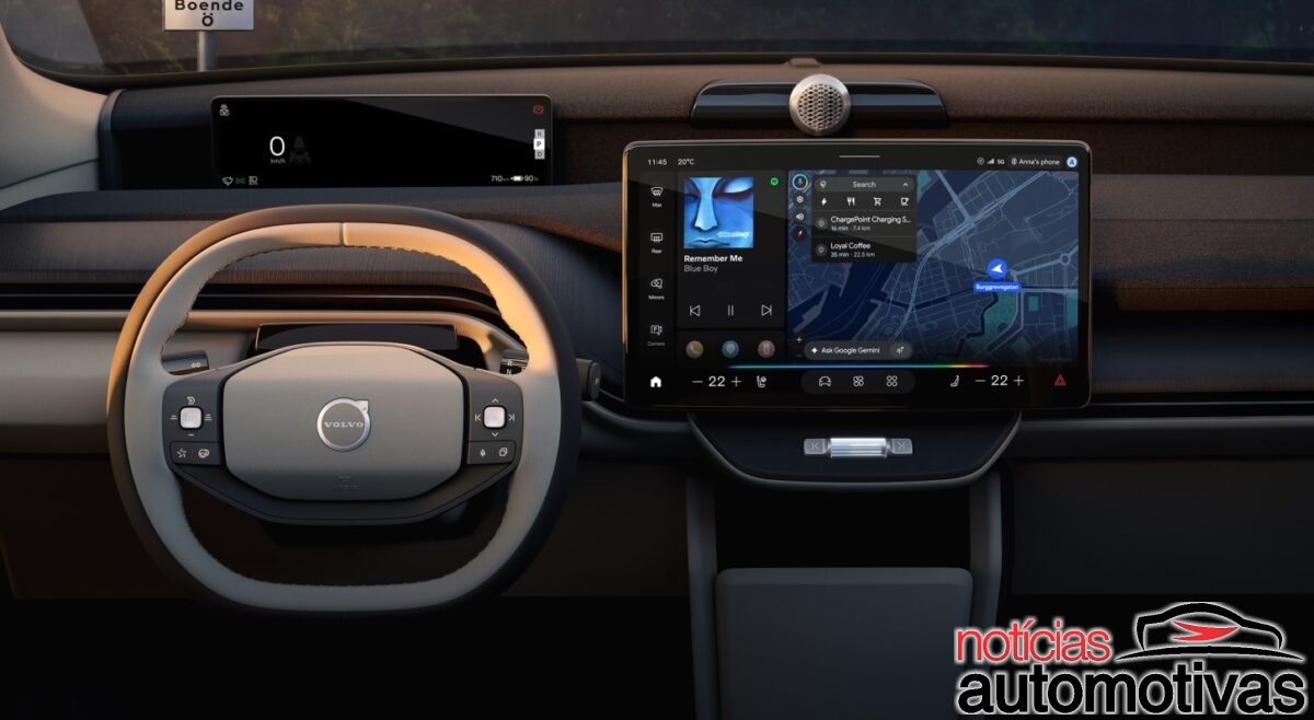 Interior de um Volvo com volante em dois tons, painel escuro e tela central exibindo mapa, música e controles.