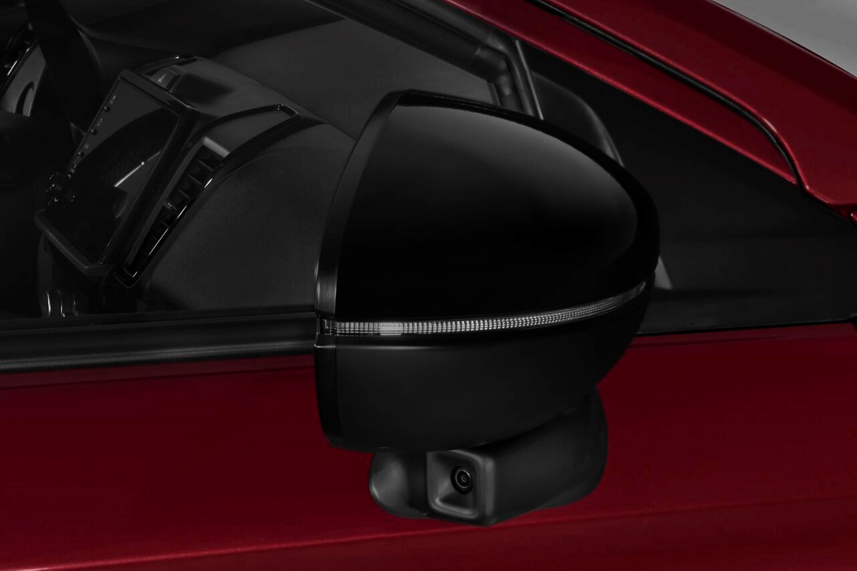 Retrovisor externo preto de um carro vermelho, com uma câmera visível na parte inferior.