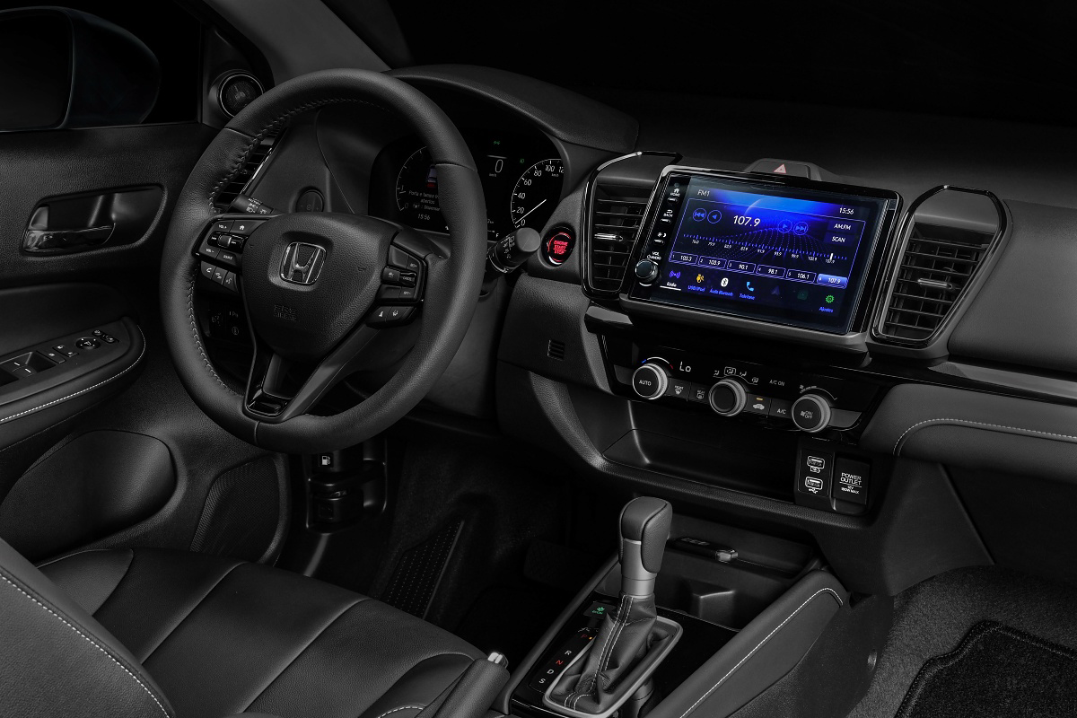 Interior dianteiro preto de um Honda, com volante, painel de instrumentos, tela multimídia e câmbio automático.