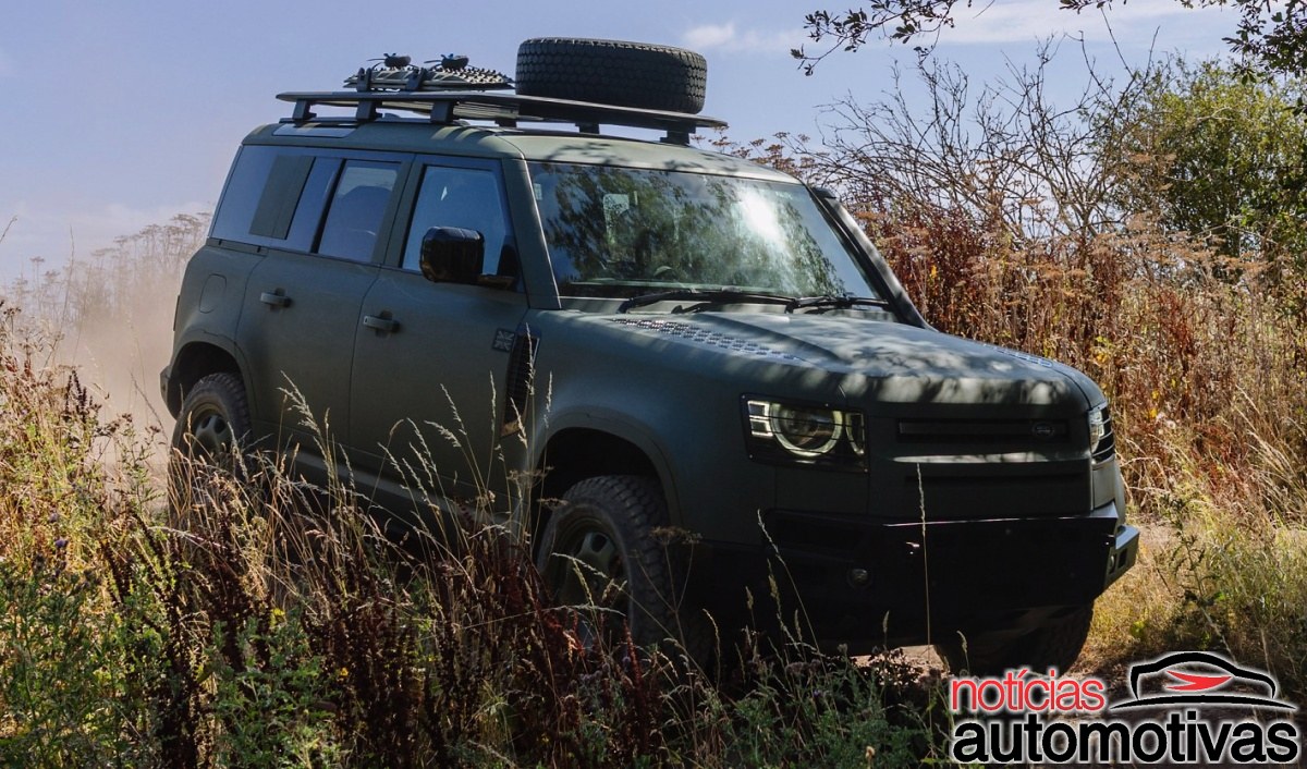 SUV verde-escuro da Defender em estrada de terra, visto de frente e pela lateral, com bagageiro e estepe no teto.
