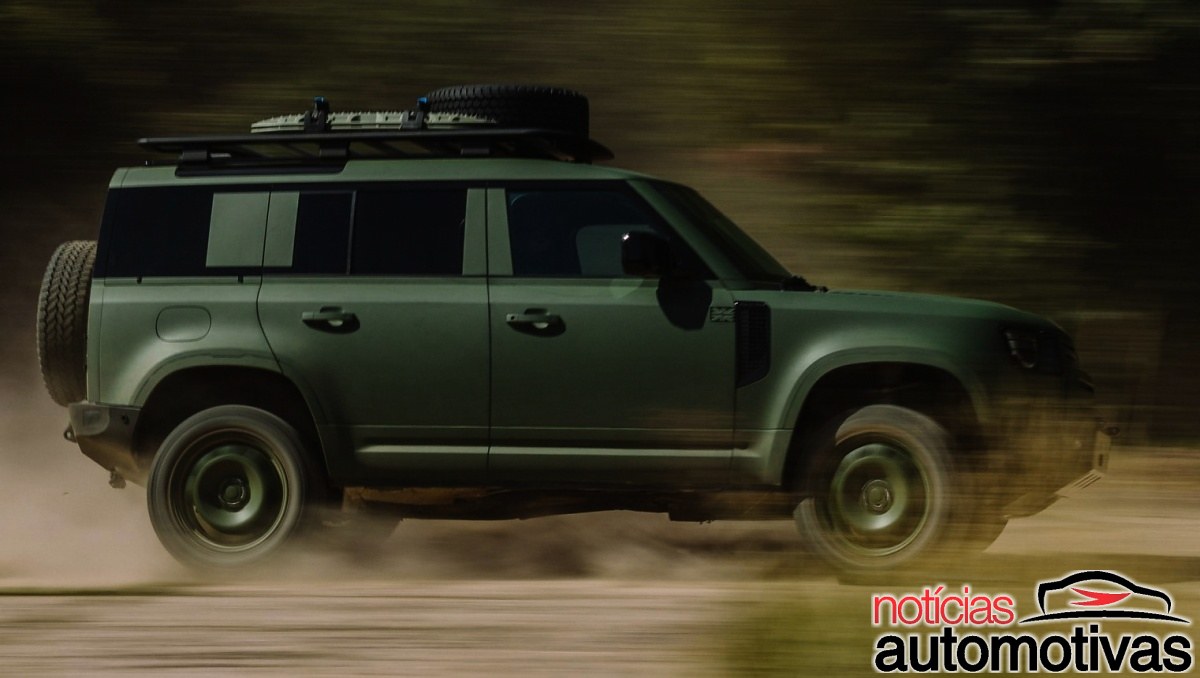 SUV verde-escuro da Defender em movimento, visto de lado, com estepe traseiro e bagageiro no teto.