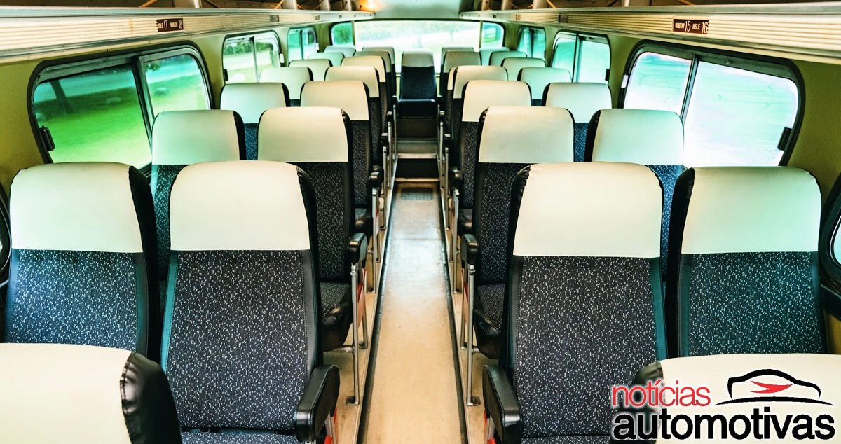 Interior do salão de passageiros de um ônibus, com fileiras de bancos e corredor central.