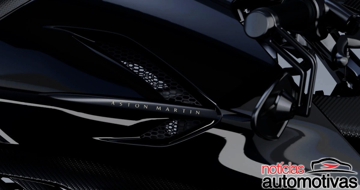 Detalhe da lateral preta de uma motocicleta com entrada de ar, textura de fibra de carbono e texto Aston Martin.