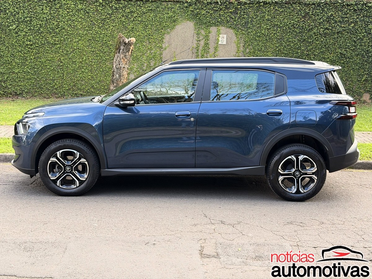 Citroën Aircross azul-escuro visto de lado, estacionado diante de um muro coberto por vegetação.