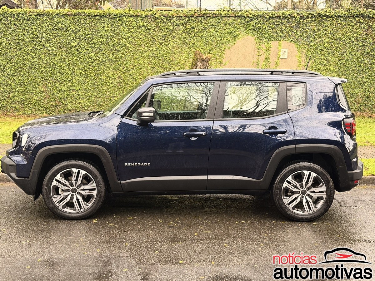 Jeep Renegade azul escuro visto de lado, estacionado diante de um muro coberto por vegetação.