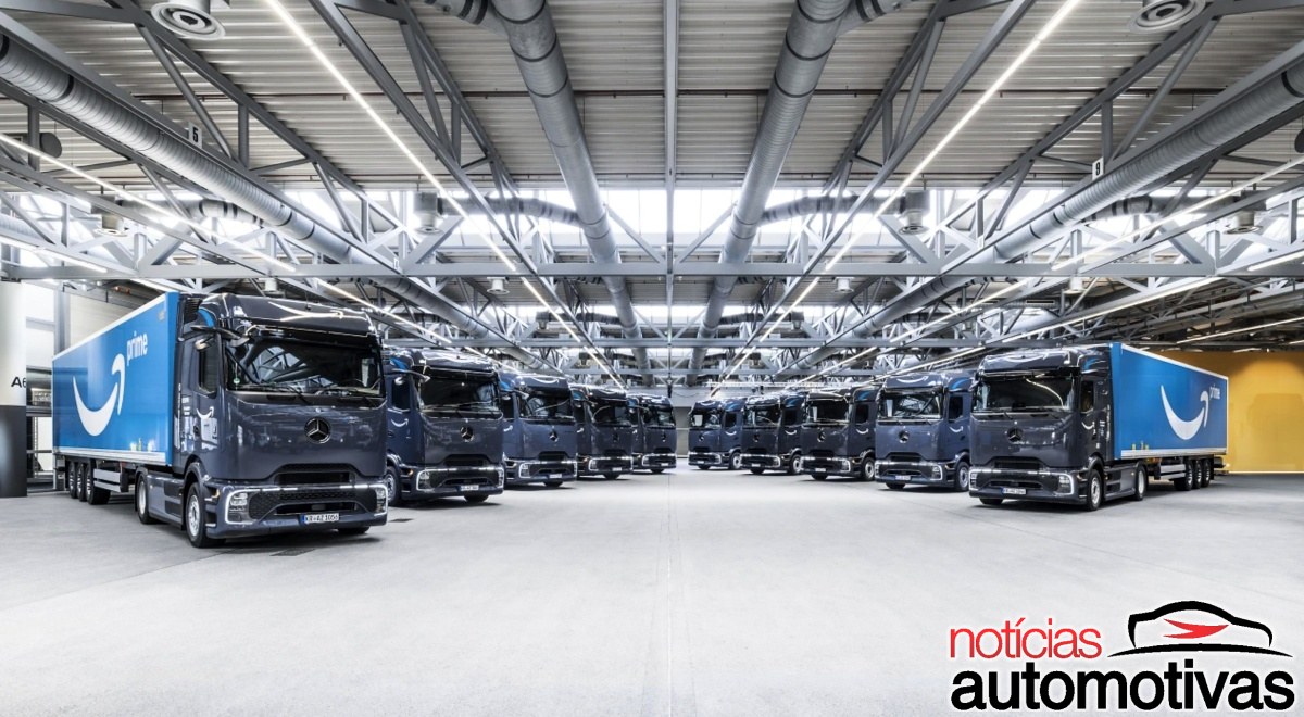 Vários caminhões Mercedes-Benz azul-escuros com baús azuis da Amazon estacionados em um galpão.