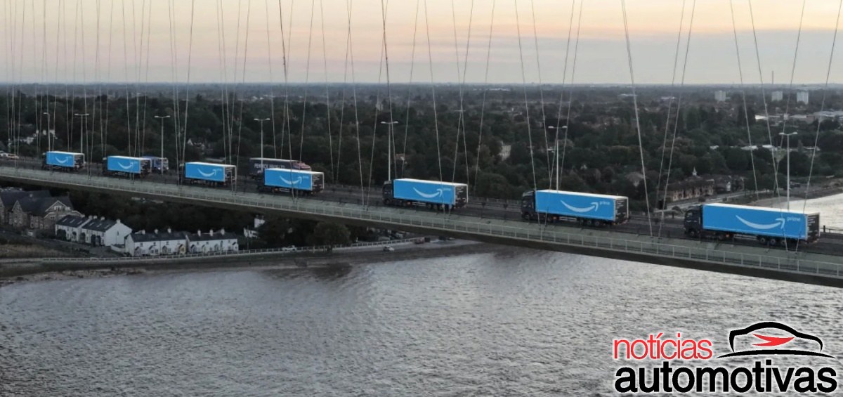 Caminhões com baús azuis da Amazon atravessam uma ponte sobre uma área de água.