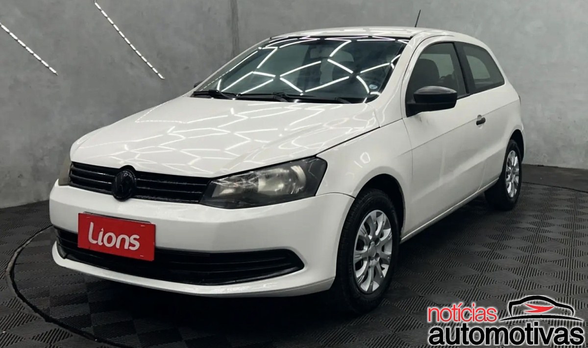 Volkswagen Gol branco de duas portas visto de frente em um ambiente interno com piso quadriculado.