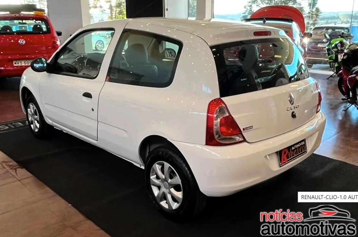 Renault Clio branco de duas portas visto pela traseira em um showroom, com o nome Clio visível.
