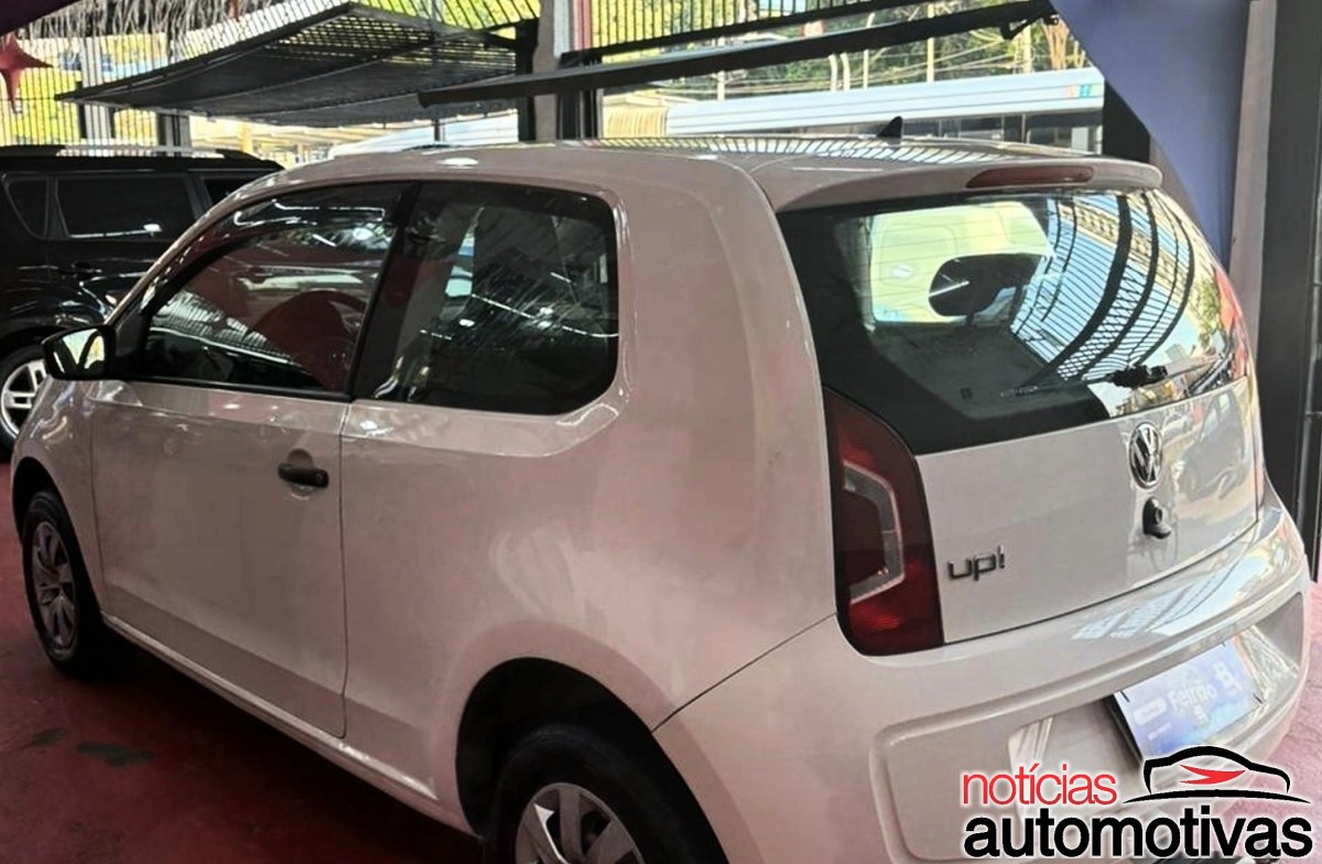 Volkswagen Up! branco de duas portas visto pela traseira e pelo lado esquerdo em uma área coberta.