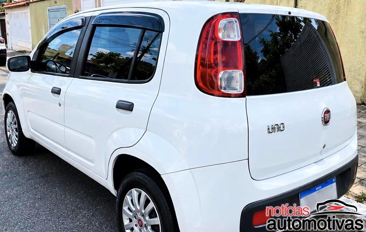 Fiat Uno branco visto pela traseira em uma rua residencial, com o emblema Uno visível na tampa.
