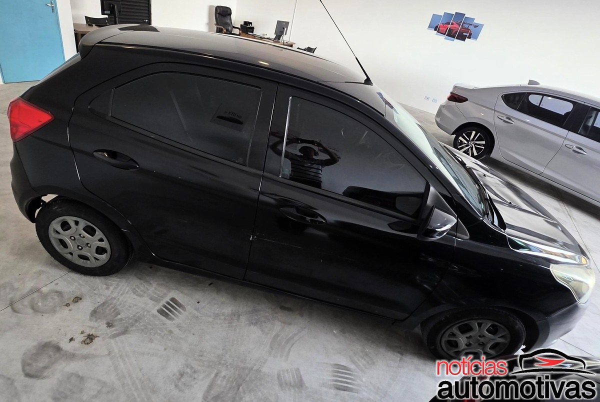 Hatch preto de quatro portas visto de cima em um showroom, ao lado de um carro branco.