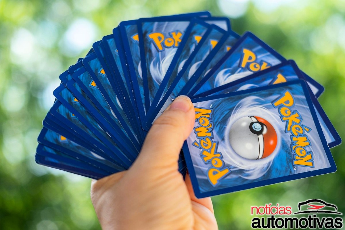 Mão segura várias cartas Pokémon abertas em leque, mostrando os versos azuis com uma Poké Bola.