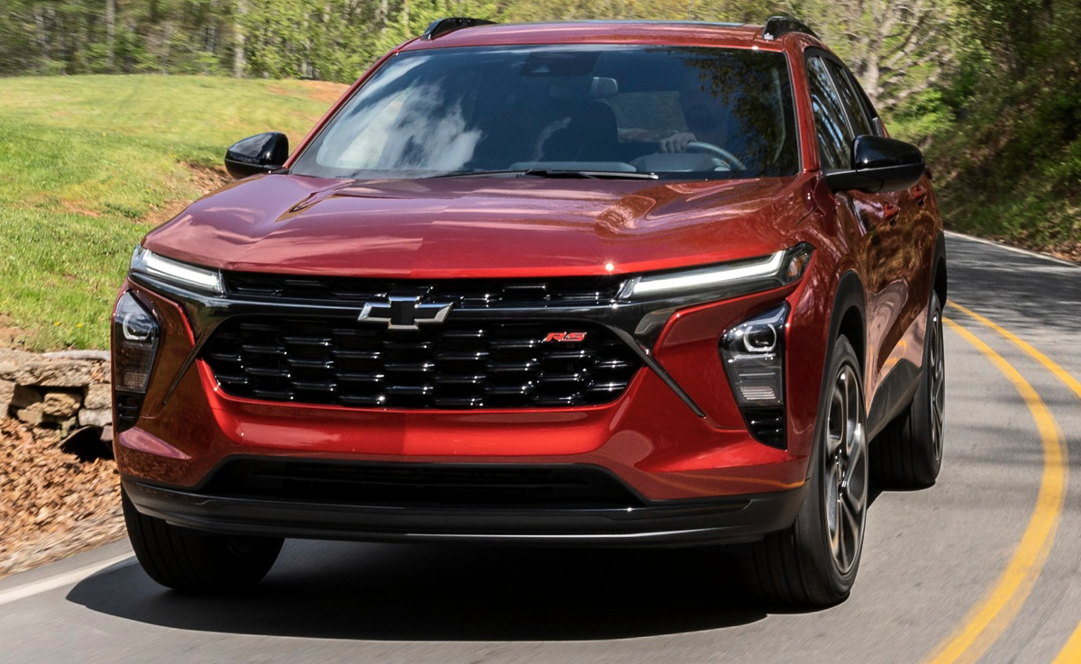 Chevrolet Trax vermelho visto de frente em uma estrada cercada por árvores e gramado.