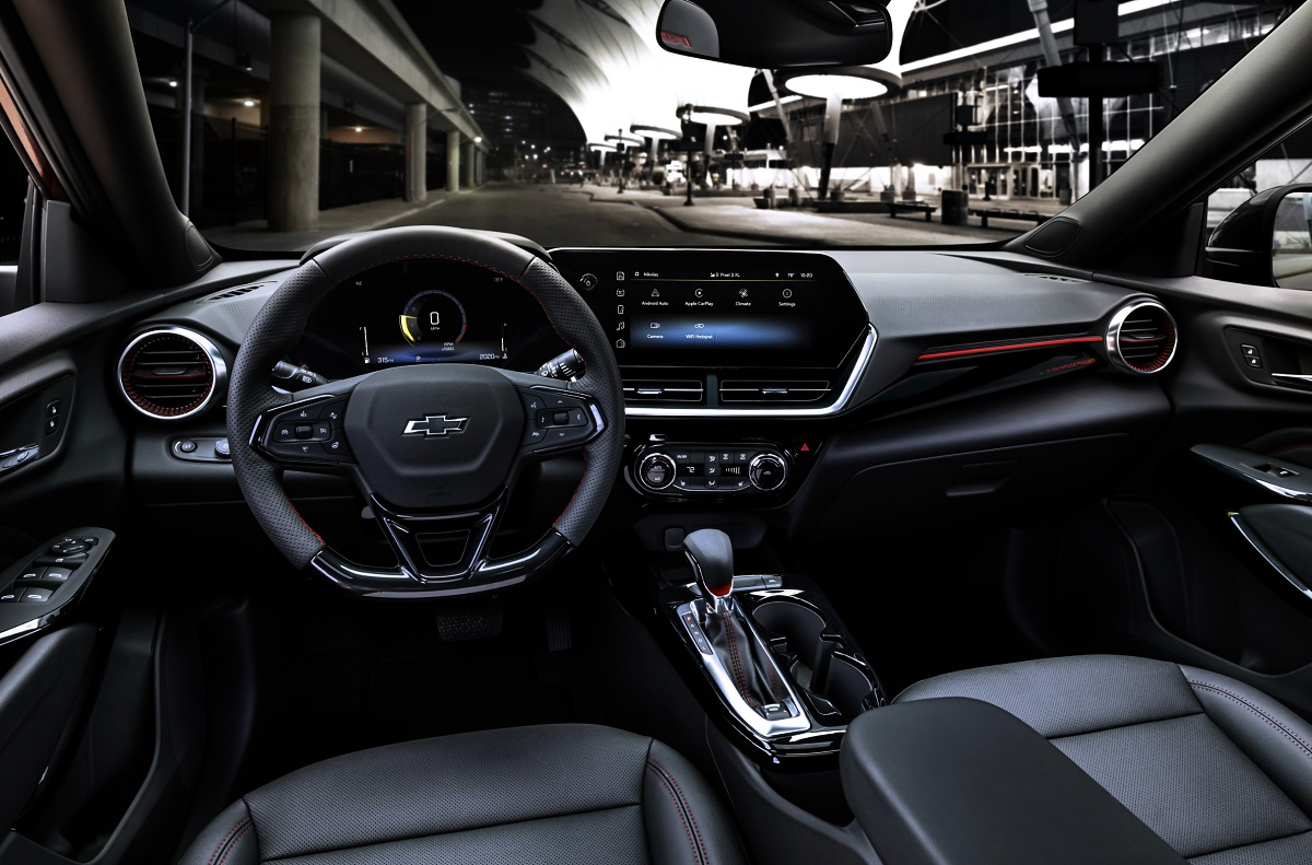 Interior dianteiro de um Chevrolet Trax, com volante, painel digital, tela central e bancos pretos.