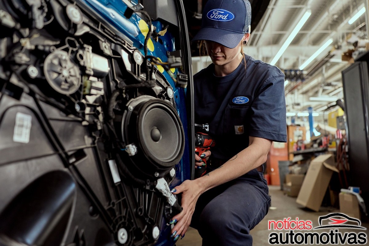 Mulher usando boné e uniforme da Ford trabalha na lateral interna de um veículo com uma ferramenta elétrica.