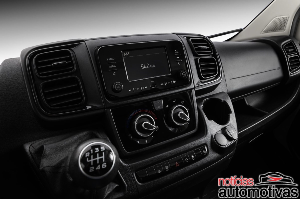 Console central da Fiat Ducato com tela de rádio, comandos do ar-condicionado, porta-copos e alavanca de câmbio manual.