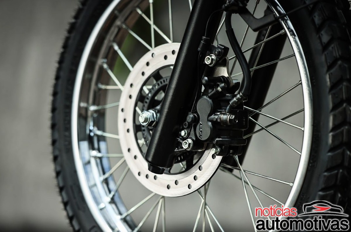 Detalhe da roda dianteira raiada de uma motocicleta, com disco de freio e pinça preta.