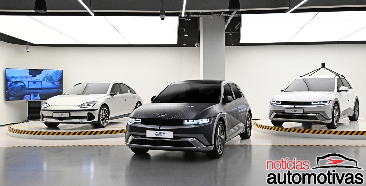 Três veículos Hyundai em uma sala de exposição: dois brancos e um escuro, com sensores no teto do modelo à direita.