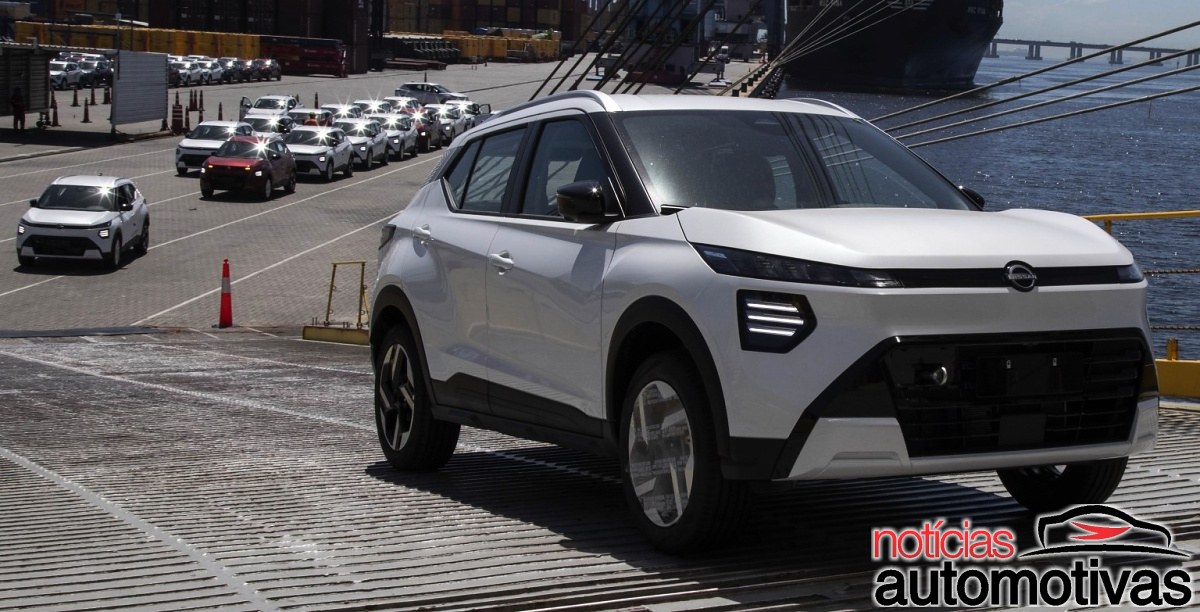 Nissan Kait branco em área portuária, com vários veículos alinhados ao fundo, um navio e água ao lado.