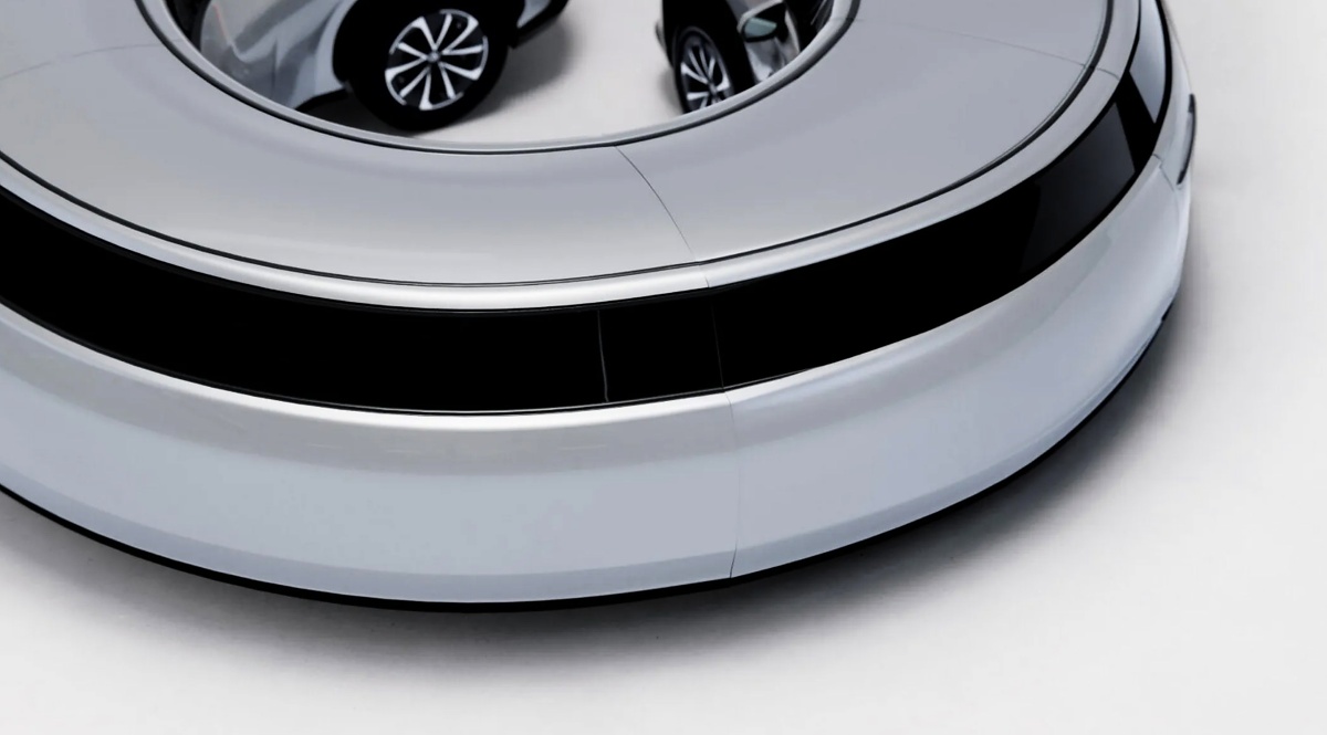 Detalhe de uma estrutura automotiva prateada em formato circular, com faixa preta e rodas visíveis ao fundo.