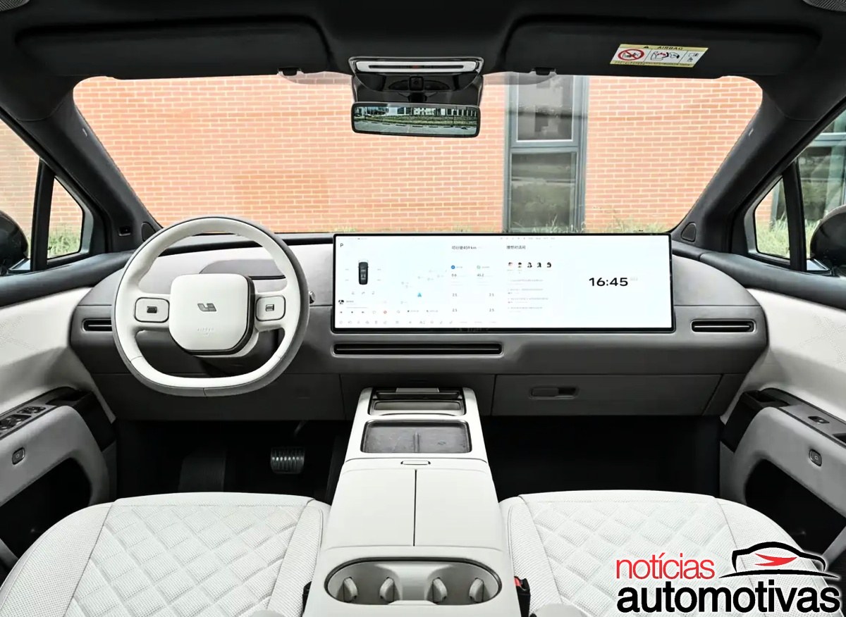 Interior dianteiro com volante branco, painel escuro e uma ampla tela central sobre o console.