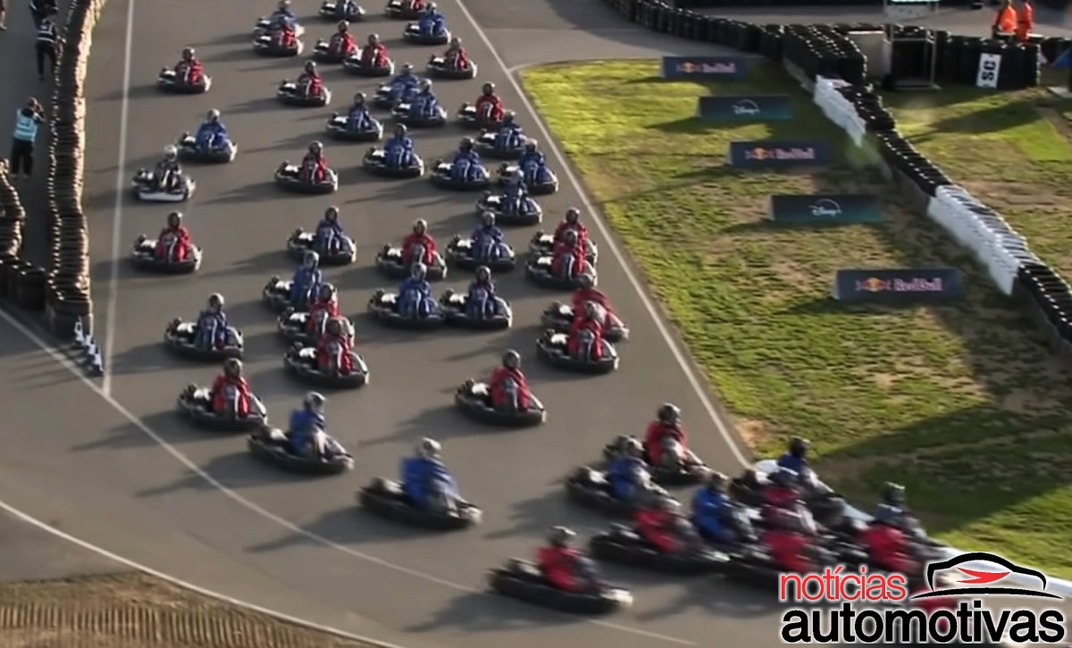 Vista elevada de vários karts em uma pista cercada por barreiras de pneus, com placas da Red Bull e da Disney no gramado.