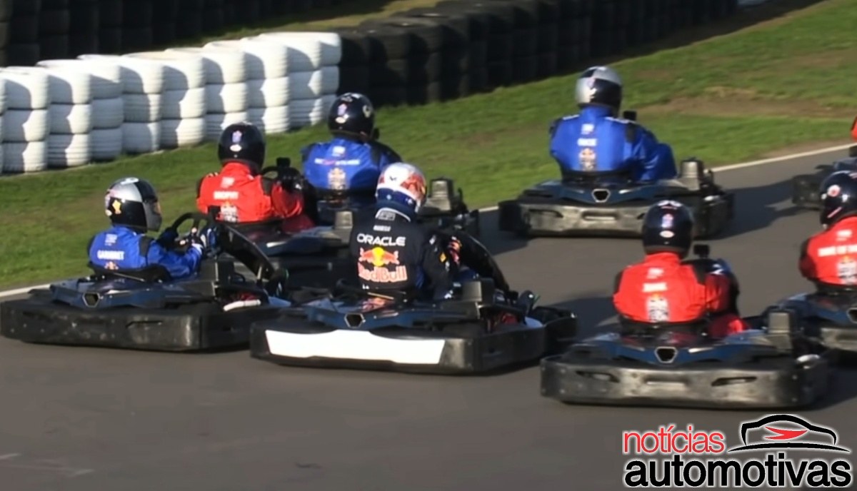 Karts com pilotos de macacões azuis e vermelhos percorrem uma curva; o piloto central usa uniforme com marcas Oracle e Red Bull.