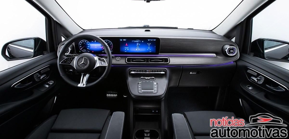Painel dianteiro preto da Mercedes-Benz Classe V, com volante, telas digitais, comandos centrais e iluminação ambiente azul.