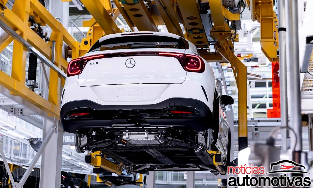 Traseira de um Mercedes-Benz GLA branco suspenso em uma estrutura amarela na linha de montagem.