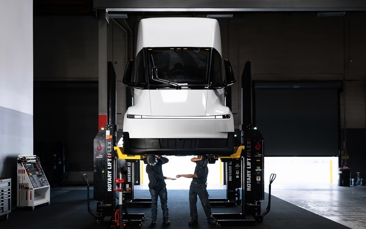 Caminhão Tesla Semi branco elevado em um elevador automotivo, com dois mecânicos sob a cabine.