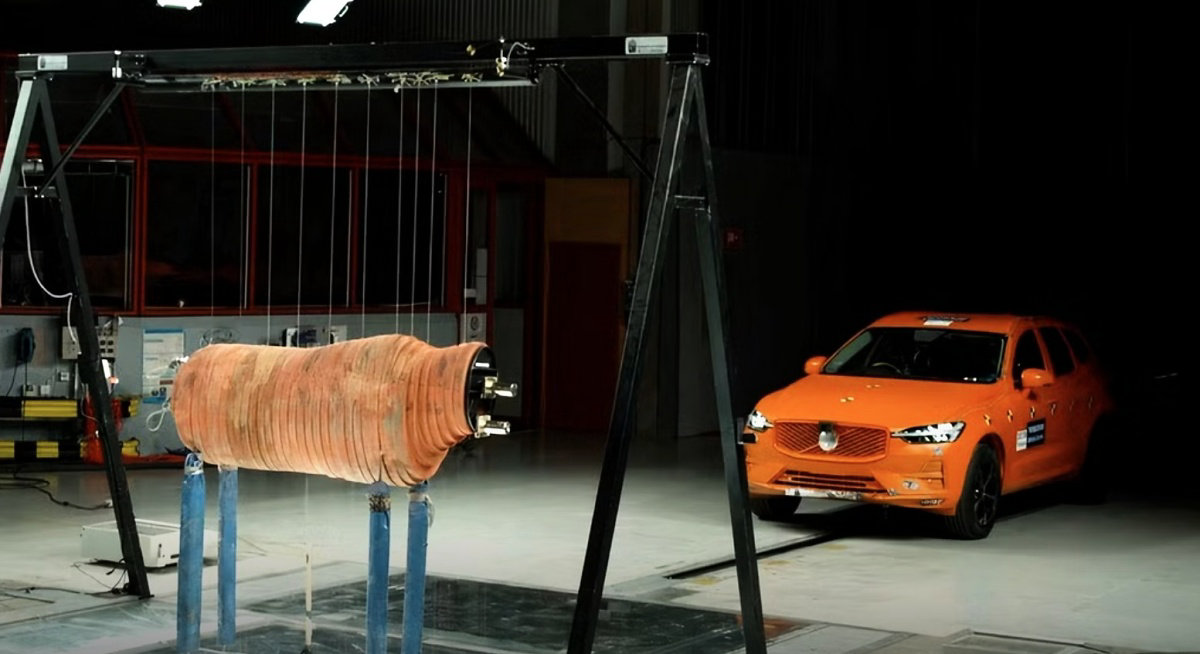 Boneco de alce suspenso diante de um SUV Volvo laranja em um laboratório de testes.