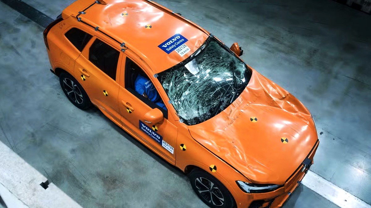 SUV Volvo laranja com para-brisa quebrado e capô amassado, visto de cima em um laboratório.