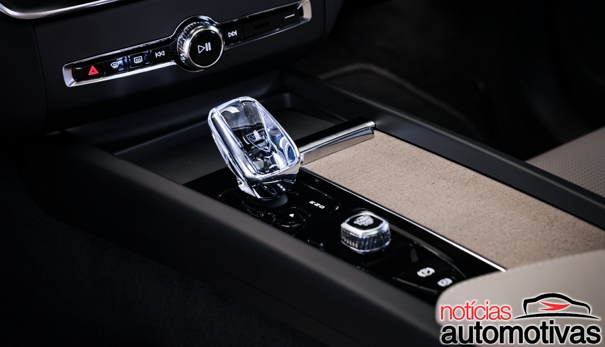 Console central de um Volvo, com seletor de câmbio transparente, controles físicos, botão giratório e acabamento escuro.