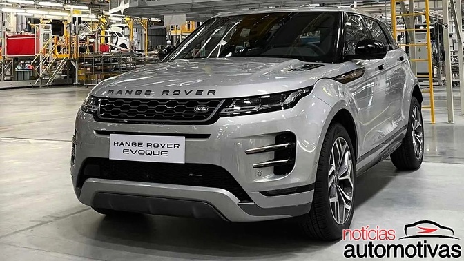 Evoque 001 Range Rover Evoque prata em uma área industrial, com máquinas e estruturas ao fundo.