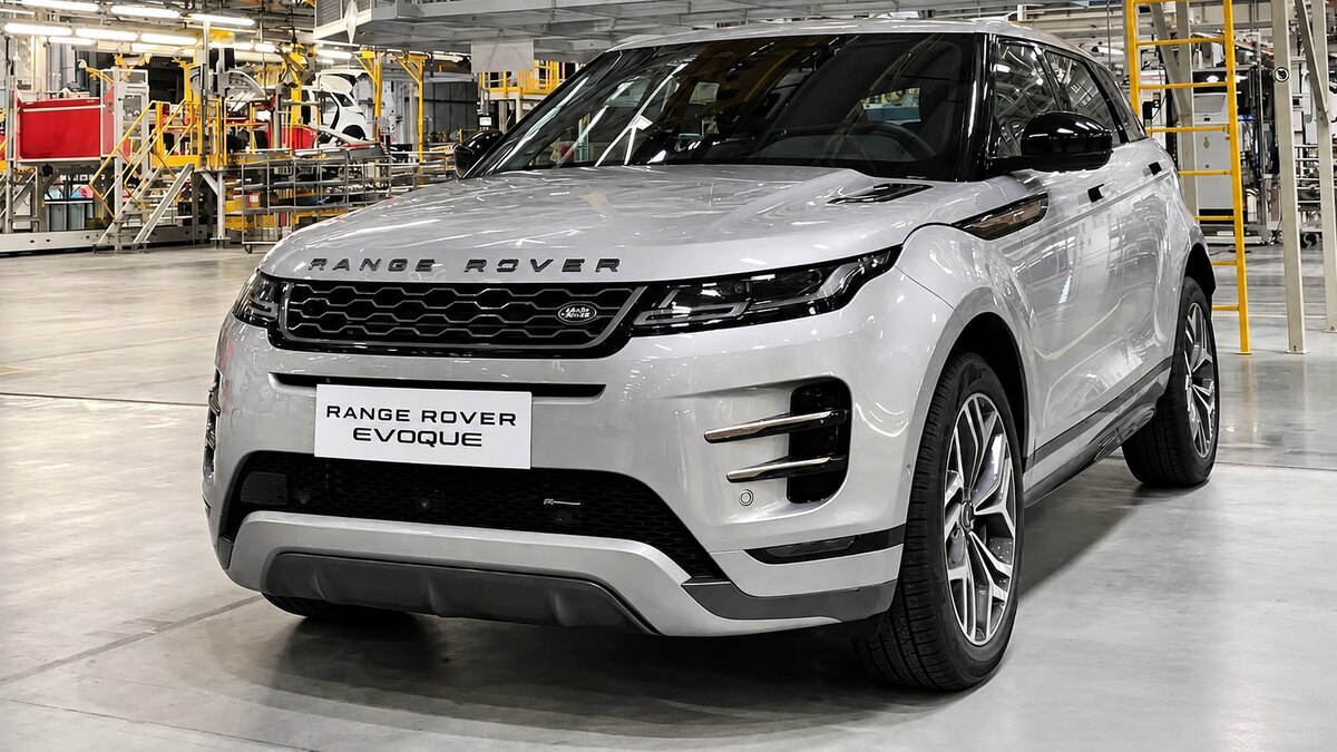 Range Rover Evoque prata em uma área industrial, com máquinas e estruturas ao fundo.