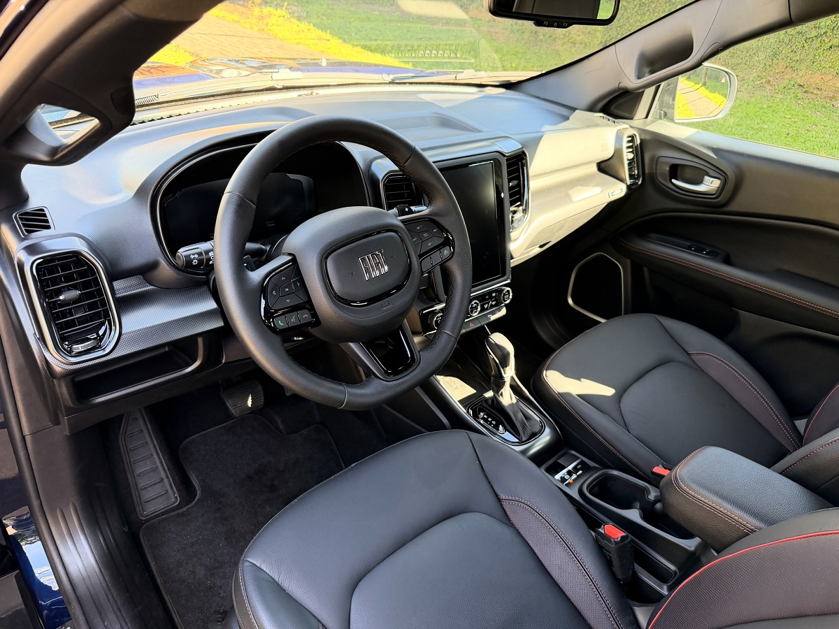 Interior dianteiro com volante Fiat, painel, tela central vertical, câmbio automático e bancos pretos com costuras vermelhas.