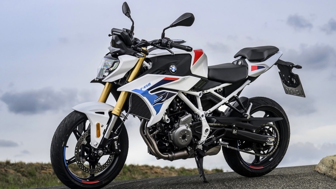 BMW F 450 R branca com detalhes azuis e vermelhos, estacionada em uma estrada sob céu nublado.