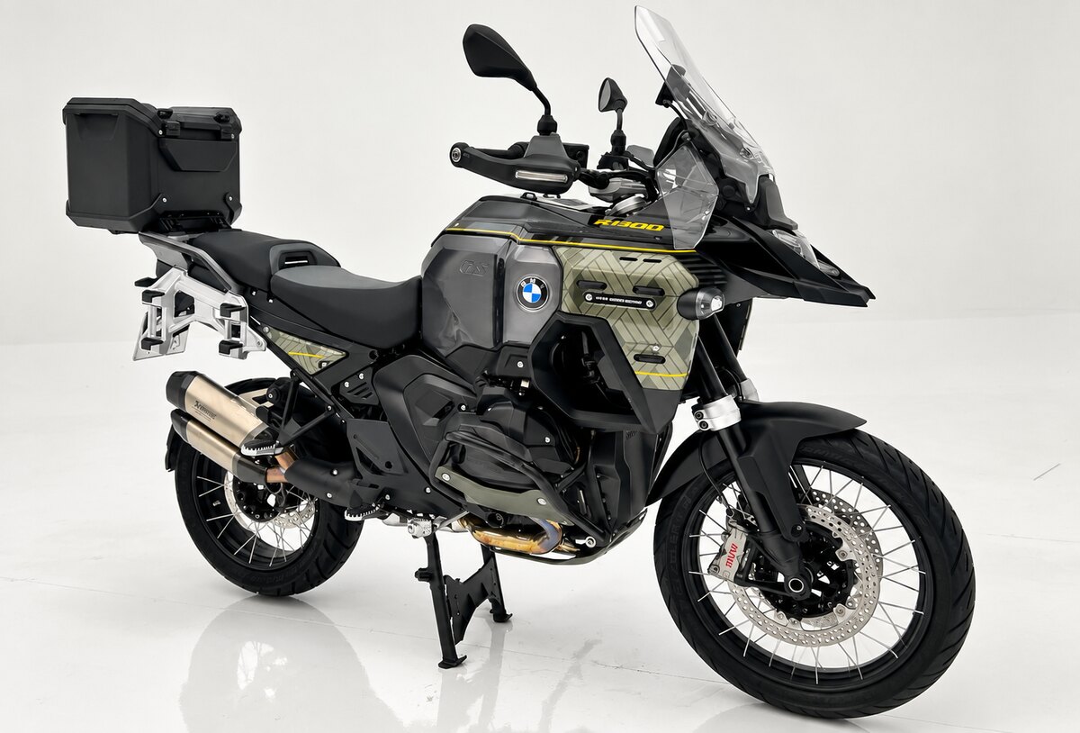 BMW R 1300 GS Adventure preta e cinza, com detalhes amarelos, para-brisa alto e baú traseiro, em fundo branco.