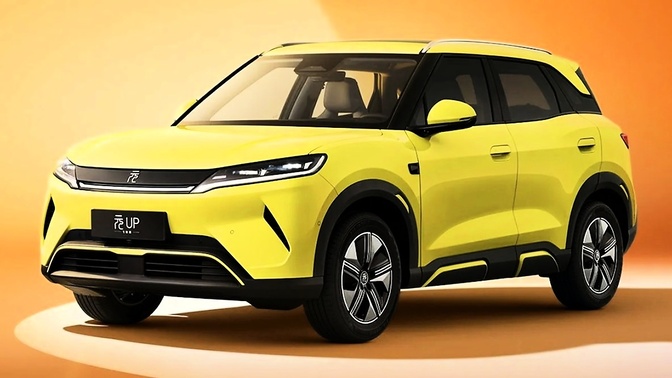SUV BYD Yuan Up amarelo, visto de frente e pela lateral, em um estúdio com fundo laranja.