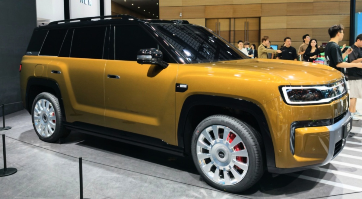 Fang Cheng Bao Ti 9 dourado visto de dianteira e lateral, com teto preto, faróis retangulares e rodas grandes, em um salão.