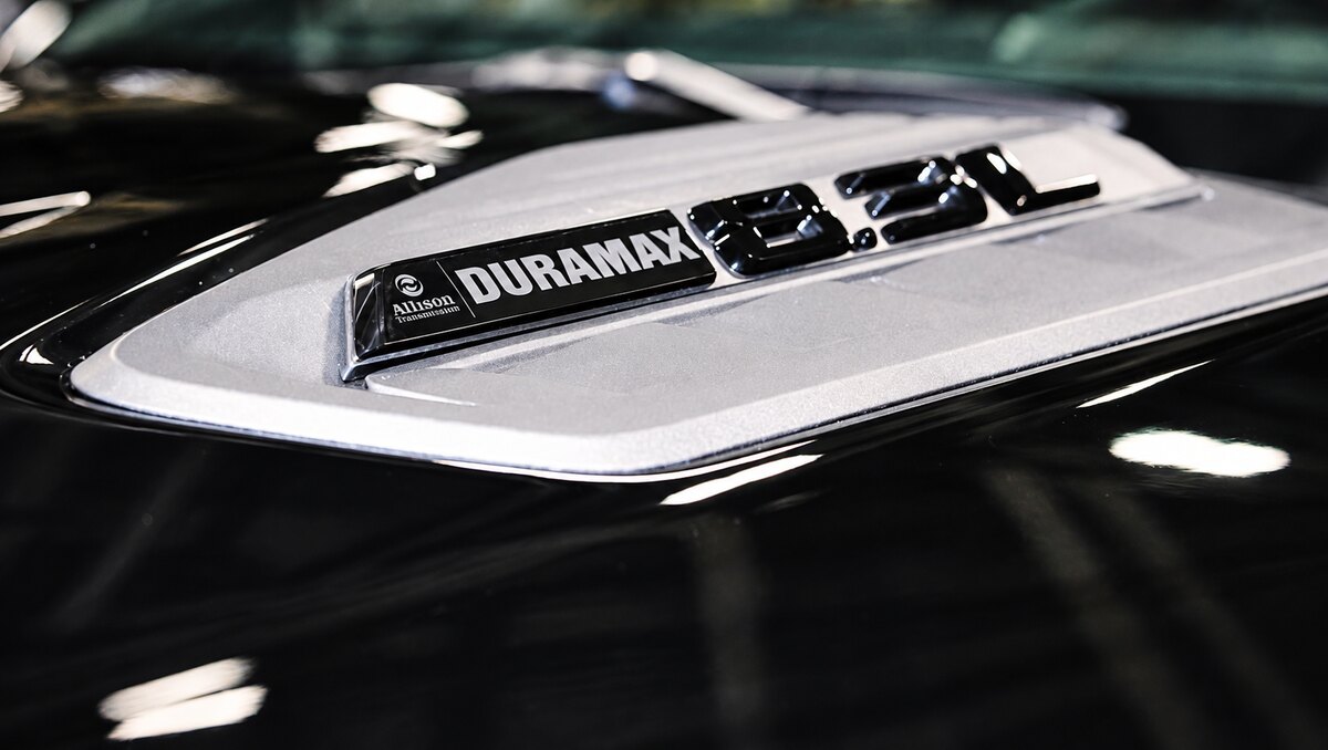 Emblema Duramax e Allison sobre um painel prateado, cercado por uma superfície preta.