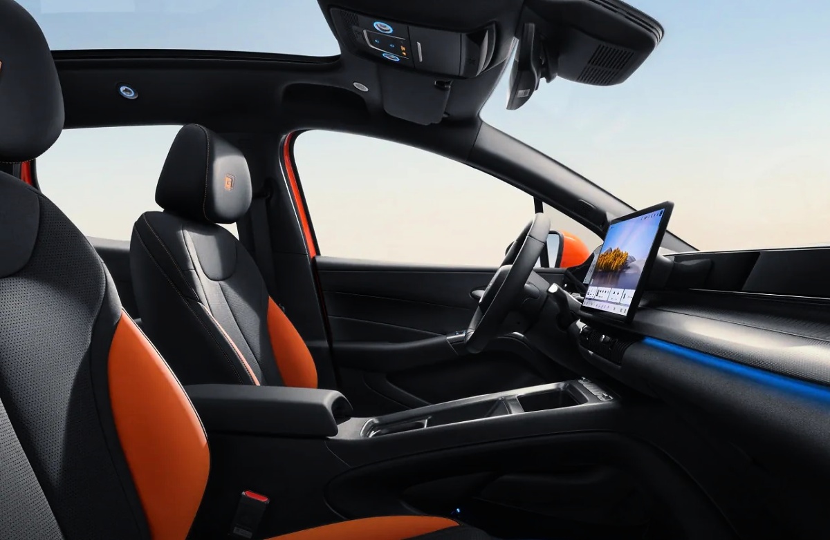 Interior do BYD Dolphin G com bancos pretos e laranja, volante e tela central vertical.