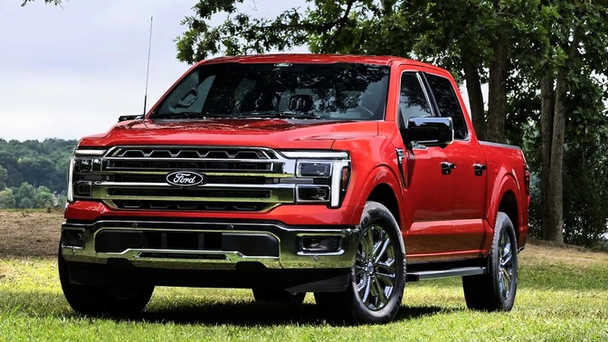 Ford F-150 vermelha vista de frente, estacionada sobre a grama, com árvores ao fundo.