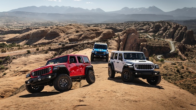 Três SUVs Jeep, nas cores vermelha, azul e branca, sobre formações rochosas; ao fundo, montanhas e céu azul.