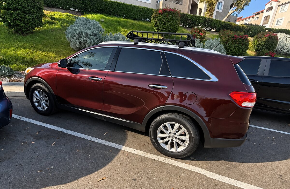 Kia Sorento bordô visto de lado, estacionado junto à calçada, com bagageiro de teto.