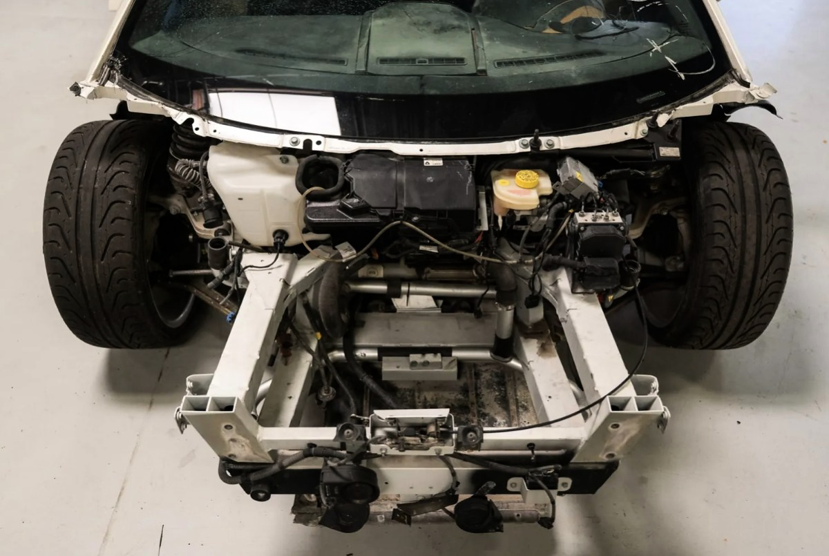 Parte dianteira desmontada de um Lamborghini Gallardo branco, com suspensão, reservatórios e componentes elétricos visíveis.