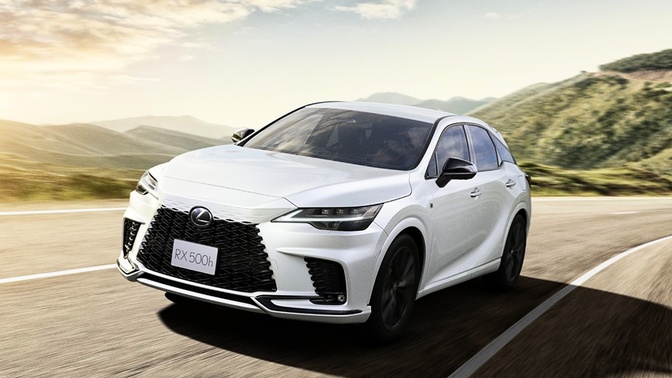 lexus-rx-500h-japão-1 Lexus RX 500h branco em movimento numa estrada, visto de frente e pela lateral, com montanhas e vegetação ao fundo.