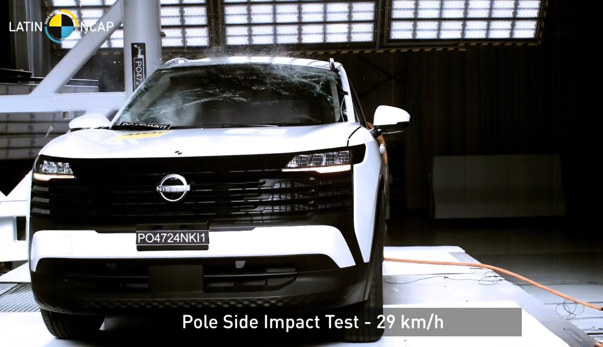 SUV branco visto de frente em área de testes; há um logotipo Nissan na grade e o texto Pole Side Impact Test – 29 km/h.