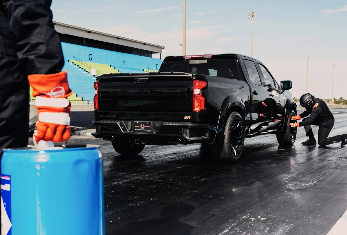 Chevrolet Silverado preta vista de traseira em uma pista, com duas pessoas ao redor e um tambor azul em primeiro plano.